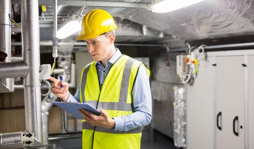 Die Betriebsmittelprüfung kann Leben retten Mann mit Sicherheitsweste und Helm prüft technische Anlage