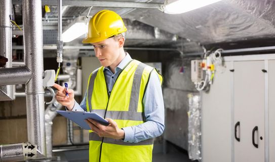 Die Betriebsmittelprüfung kann Leben retten Mann mit Sicherheitsweste und Helm prüft technische Anlage