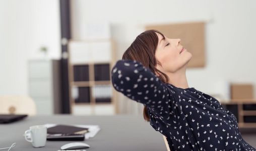 Keinen Stress aufkommen lassen Frau sitzt entspannt und zurückgelehnt am Schreibtisch